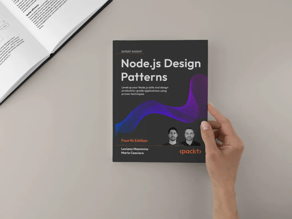 Hand holding the 'Node.js Design Patterns – Fourth Edition' book on a beige desk next to an open book; front cover with the purple wave motif clearly visible.